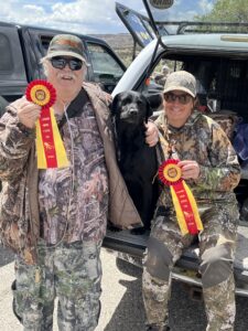 a man and woman in camouflage holding ribbons with a dog 